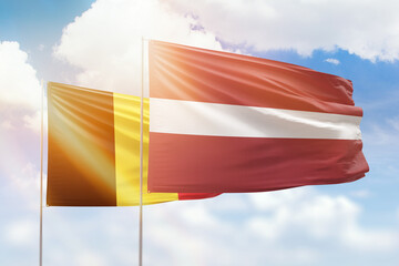Sunny blue sky and flags of latvia and belgium