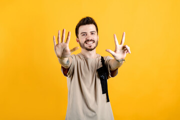 Young man smiling confident wearing beige tee posing isolated over yellow background showing and pointing up with fingers number eight while smiling.