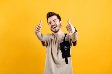Fototapeta premium Portrait of man wearing beige tee posing isolated over yellow background doing hand gesture for great accomplishment. Show two hands thumbs up have good mood.
