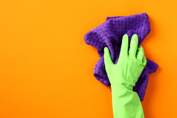 Female hand in protection glove with cleaning rag on orange background - obrazy, fototapety, plakaty