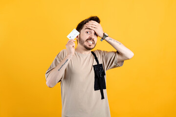 Caucasian man wearing beige tee posing isolated over yellow background showing credit card stressed...