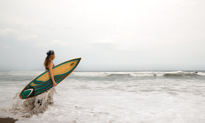 caucasian surfer woman holding a surfboard and entering the sea ready to surf the waves