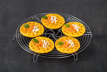 Small  round carrot waffles on a serving stand. Dark gray background