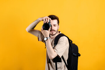 Obraz premium Caucasian young man wearing t-shirt posing isolated over yellow background taking images with dslr camera. Photographer covering his face with the camera.