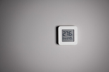 Electronic indoor white plastic digital thermometer on gray wall showing temperature, humidity...