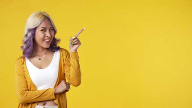Young asian woman pointing fingers up at empty copy space for text isolated on yellow background