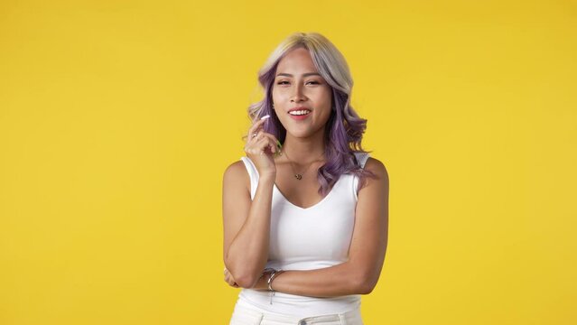 Thinking young Asian woman standing isolated over yellow background