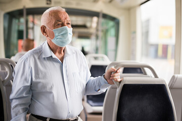 Old European man in face mask standing in streetcar and waiting for next stop.