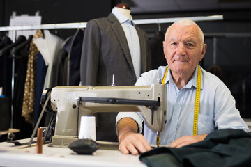 Portrait of elderly man tailor working on sewing machine at studio