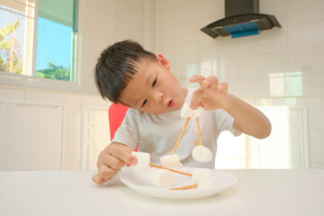 Cute little Asian 5 years old kindergarten boy child sitting at the kitchen building tower with...