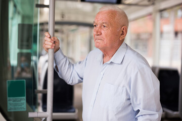 Old European man standing in streetcar and waiting for next stop.