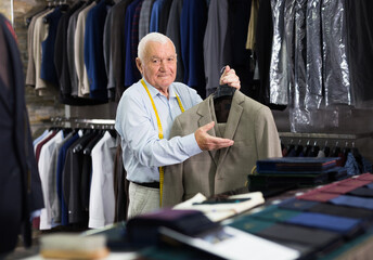 Mature male tailor demonstrating of fashionable suit in apparel shop