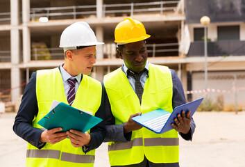 Two qualified civil engineers, standing on the construction site, controls the progress of work on...