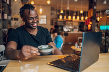 Fototapeta na wymiar African american man using laptop while drinking coffee in a cafe