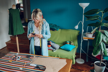 Woman tailor using a smartphone while working in her tailoring studio