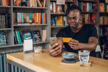 Fototapeta premium African american man using smartphone and credit card in a cafe