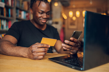 African american man using smartphone and credit card in a cafe