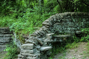 A dry laid curving stone wall in a wooded park. - obrazy, fototapety, plakaty