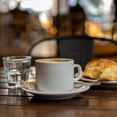 a cup of coffee with a croissant on a table in a bar