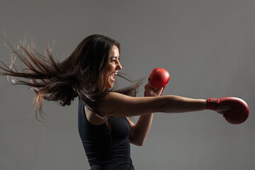 beautiful girl exercising karate punch and screaming against gray background. .