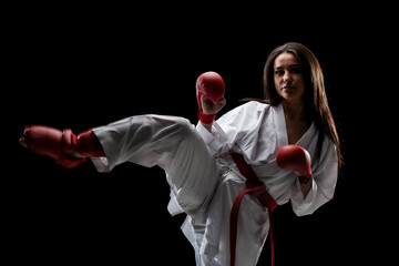 girl exercising karate leg kick wearing kimono and red gloves against black background.. © Nikola Spasenoski