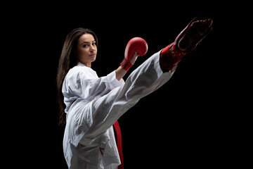 girl exercising karate leg kick wearing kimono and red gloves against black background..