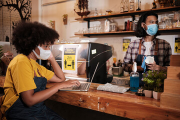 Two young cafe barista partners and entrepreneur work with face mask in coffee shop, waiting for customers order in new normal lifestyle service, SME business impact from COVID19 pandemic quarantine.