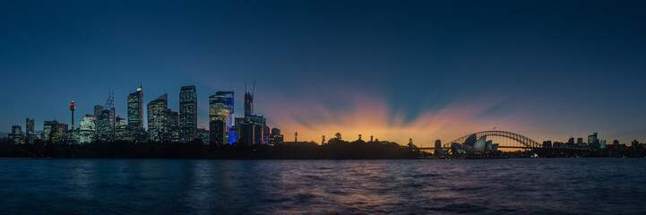 Sydney skyline and harbour after sunset with opera house and bridge in rays of dusk light