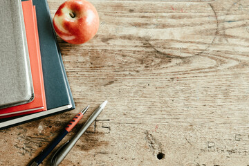 Stack of red and blue books and pencils with a red apple on a rustic weathered school desk with copy space - Powered by Adobe