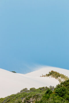 sand drifting on white dunes under blue sky vertical