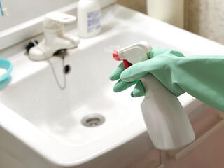 洗面台の掃除をするビニール手袋をして洗剤を持つ手2