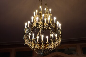 Splendid candelabra with multiple branches, interior detail in luxorious historic hall, electric light bulbs in shape of candles, brass, crystal