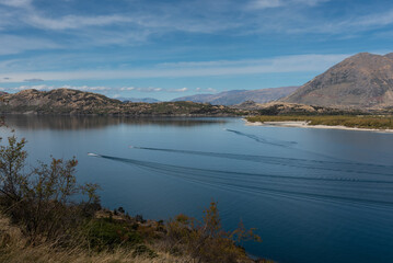 Elavated view of Lake Wanaka with three motor boats cutting through the calm surface and leaving...