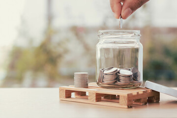Coins in a glass bottle, Hand of male or female putting coins in jar with money stack step growing...