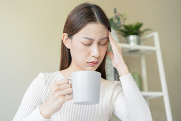 Fatigue, tension asian young woman having headache, migraine after drinking caffeine of coffee or...