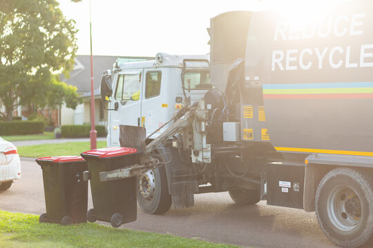 Garbage truck picking up bins from curb side in suburban area