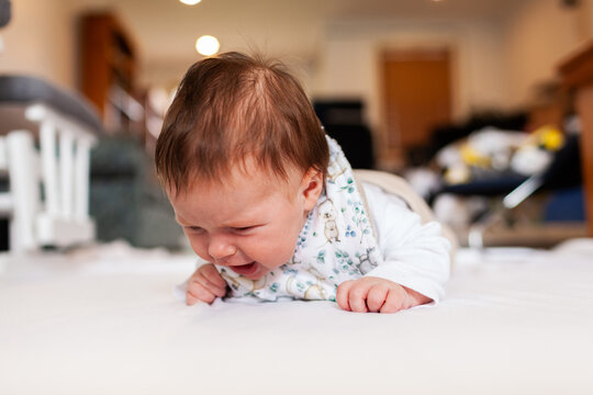 Two month old baby doing tummy time on white mat with copy space