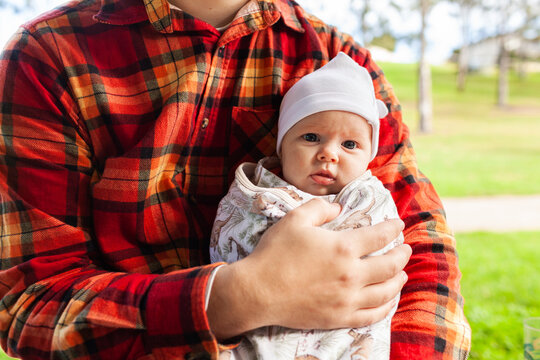 Father holding baby at park wrapped up in blanket and cap to keep warm in winter