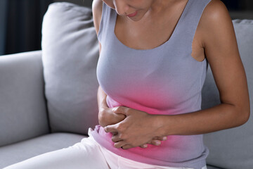 Young Asian woman having a stomach ache. Menstrual period cramp, abdominal pain, food poisoning. Health care and medical concept.
