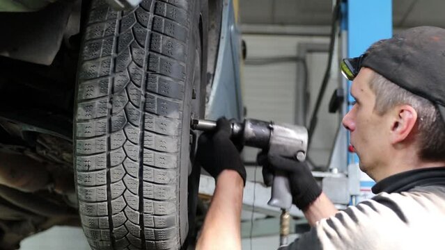 A man tightens the bolts on the wheel with an air gun, in a car service
