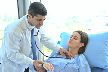 The doctor examines the stethoscope and checks the lungs of the heart of a female patient lying on the patient's bed.