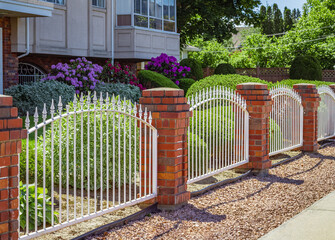 Metal white fence with brick pillars. Forged fence on red brick pillars