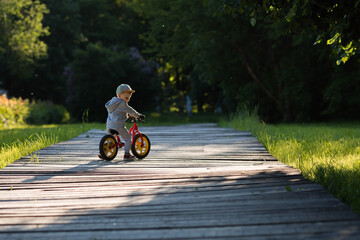 Funny little boy riding a bicycle (running bike) outdoors. A happy child walks in the spring park....