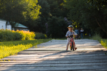 Funny little boy riding a bicycle (running bike) outdoors. A happy child walks in the spring park. The kid is dressed in a tracksuit and sneakers.