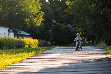 Fototapeta premium Funny little boy riding a bicycle (running bike) outdoors. A happy child walks in the spring park. The kid is dressed in a tracksuit and sneakers.