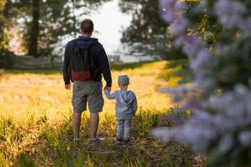 A man and a boy go hiking in the summer forest with a backpack for hiking. Portrait of a father and son sitting on his father's shoulders in the forest at sunset. The concept of travel.