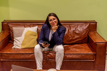 Portrait of young white woman in a busy modern workplace working and  holding phone or tablet in a...