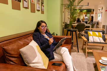 Portrait of young white woman in a busy modern workplace working and  holding phone or tablet in a...