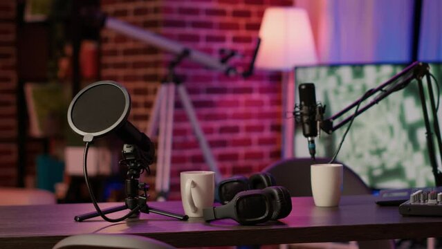 Closeup of headphones and professional microphone on empty vlogger desk ready for live talk show broadcast on internet. Detail of equipment for dual vlog on empty desk for online podcast streaming.