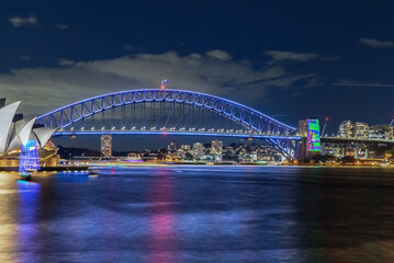 Naklejka na ściany i meble Colourful Light show at night on Sydney Harbour NSW Australia. The bridge illuminated with lasers and neon coloured lights. Sydney laser light show